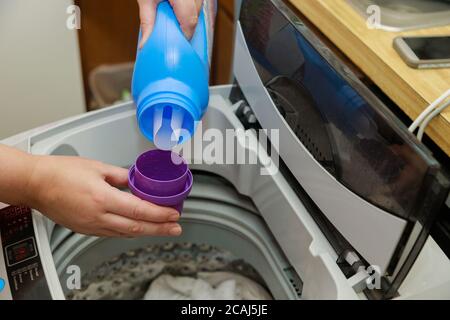 Femme verse de la poudre de savon liquide dans le tambour du linge de la machine à laver Banque D'Images