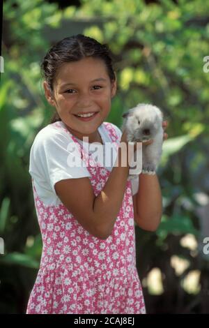 Austin Texas USA,1995: Fille hispanique de 9 ans tient doucement son lapin de lapin d'animal de compagnie dans l'arrière-cour de sa famille. M. EC-0089 ©Bob Daemmrich Banque D'Images