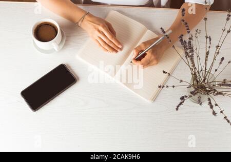Une femme écrit dans un carnet tout en étant assise dans la pièce à la table. Banque D'Images