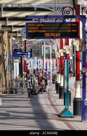 Les passagers quittant un train Northern Rail à la gare de Skipton avec un écran d'informations sur les passagers à matrice de points indiquant les heures de départ du train. Banque D'Images