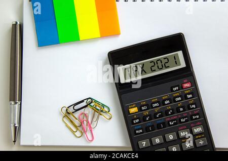 Calculatrice avec inscription « TAX 2021 », note blanche, papier de couleur, trombones, stylo. Concept d'entreprise. Magnifique arrière-plan blanc, espace de copie. Banque D'Images