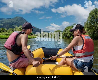 Jeune couple - homme et femme caucasiens pagayant en radeau pneumatique jaune sur la rivière de montagne Orava. Sports extrêmes et amusants en Slovaquie, en Europe centrale. Banque D'Images