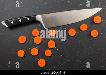 Grenaille au-dessus, tranches de carottes en petits cercles, avec couteau de chef au-dessus, sur une planche de travail en marbre noir Banque D'Images