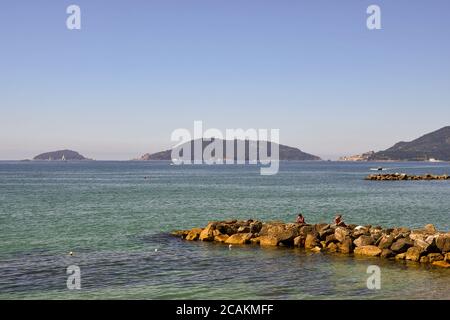 Vue sur le golfe des poètes avec des gens qui bronzer sur les rochers et l'archipel de Porto Venere (site de l'UNESCO) en arrière-plan en été, en Italie Banque D'Images