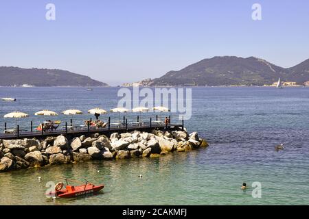 Vue sur le golfe des poètes avec les gens qui bronzer sur la rive rocheuse, le promontoire de Porto Venere et l'île de Palmaria, Lerici, Italie Banque D'Images