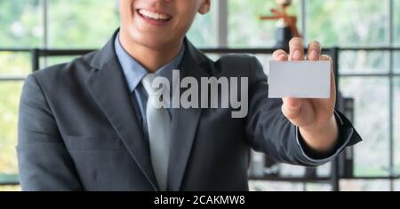 Un jeune homme d'affaires asiatique porte une tenue et montre une vue sur le devant une maquette de carte de visite blanche vierge. Concept de professionnel présentez-vous Banque D'Images