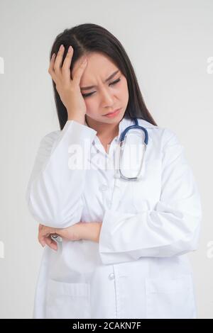 Jeune femme asiatique médecin debout et tenant les mains dans la tête en raison de maux de tête, elle semble malheureux et fatigué en raison de travail excessif, concept de stress Banque D'Images