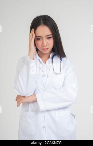 Jeune femme asiatique médecin debout et tenant les mains dans la tête en raison de maux de tête, elle semble malheureux et fatigué en raison de travail excessif, concept de stress Banque D'Images