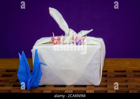 Cygnes japonais artisanaux à l'origami avec cadeau en tissu furoshiki, sur plateau en bois réutilisez les textiles et le papier pour des cadeaux durables sans gaspillage Banque D'Images