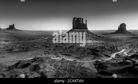 Noir et blanc photo montrant la route de gravier qui s'enroule autour de Mitten Buttes est et ouest dans le paysage désertique de Monument Valley, Utah, États-Unis Banque D'Images