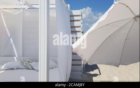 Parasol blanc et parasol sur sable de plage transparent. Mur en bois rayé peint en blanc avec ciel bleu et nuages blancs. Simplicité de la plage blanche l Banque D'Images