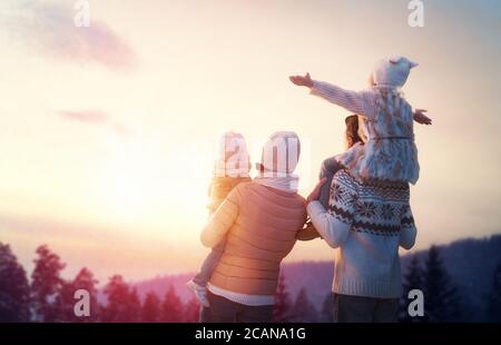 Bonne famille au coucher du soleil. Le père, la mère et deux enfants filles s'amusent et jouent sur une randonnée hivernale enneigée dans la nature. L'enfant est assis sur le sho Banque D'Images
