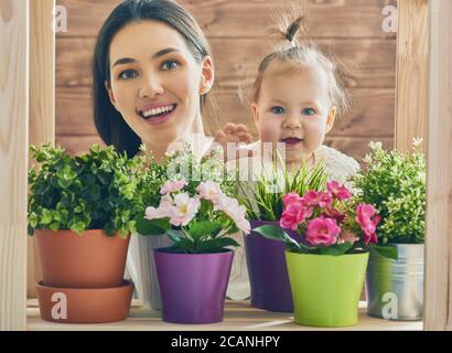 Bonne famille aimante. Mère et son enfant bébé fille jouant dans la journée d'été. Mère et fille regardent les plantes de maison et les fleurs en pot. Banque D'Images