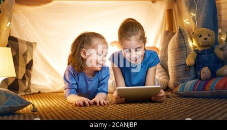 Les enfants adorables jouent avec une tablette dans une tente. Des filles heureuses à la maison. Drôle, les enfants s'amusent dans la chambre. Banque D'Images