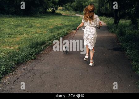 Femme dans une longue robe blanche marche avec un en été, le chaton d'animal de compagnie race Scottish Straight dans le parc Banque D'Images