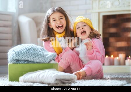 De jolies petites filles assises sur le sol et tenant des vêtements tricotés chauds. Les enfants apprécient l'hiver. Banque D'Images