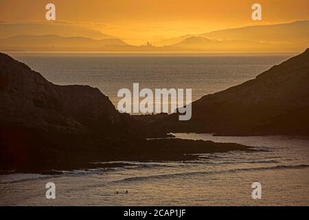 Mumbles, Swansea, Royaume-Uni. 8 août 2020. Les personnes nageant dans la mer calme tandis que le soleil se lève sur le phare de Mumbles près de Swansea ce matin au début d'une journée d'été du Royaume-Uni. Credit: Phil Rees/Alamy Live News Banque D'Images