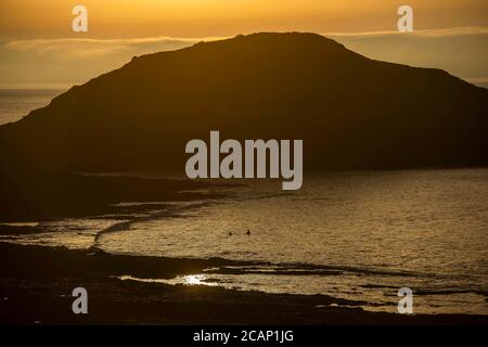 Mumbles, Swansea, Royaume-Uni. 8 août 2020. Les personnes nageant dans la mer calme tandis que le soleil se lève sur le phare de Mumbles près de Swansea ce matin au début d'une journée d'été du Royaume-Uni. Credit: Phil Rees/Alamy Live News Banque D'Images