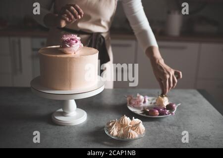 Femme faisant gâteau décorant avec des roses de fleur restant sur la table de cuisine près à la maison. Jour de mariage. Mise au point sélective. Banque D'Images