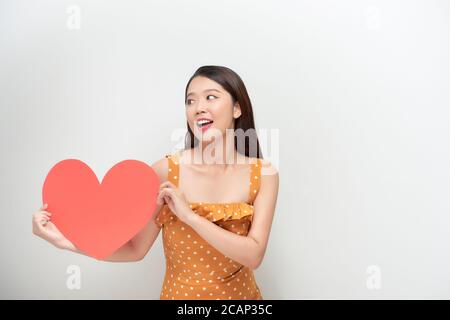 Concept de style de vie et de vacances - Portrait jeune femme heureuse en robe à pois tenant un grand papier coeur rouge. Banque D'Images