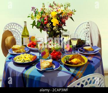 Table à manger avec fleurs, vin blanc, plats et chaises blanches Banque D'Images