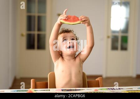 Petite fille sans chemise avoir plaisir à manger des fruits frais en été avec sa main. Banque D'Images