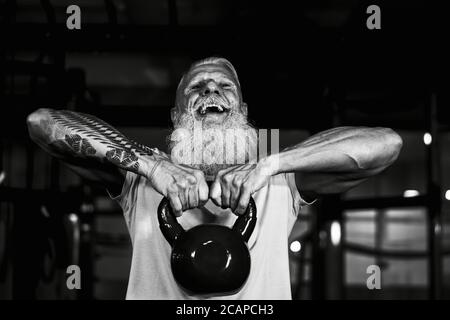 Homme de fitness senior faisant des exercices de cloche de bouilloire dans la salle de gym - Former des hommes matures dans le centre du club de bien-être Banque D'Images