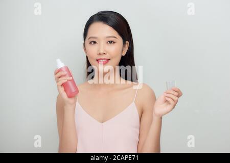 Belle femme pulvérisant sur le visage isolé sur fond blanc Banque D'Images