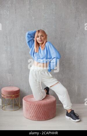 Portrait d'une jeune femme portant un pantalon déchiré vêtements de sport debout à mur en béton Banque D'Images