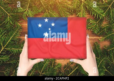 Boîte avec drapeau Samoa dans les mains des femmes. Branches de sapin sur l'arrière-plan Banque D'Images