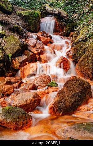 Détail des sources minérales. Cascade sur un ruisseau d'eau minérale avec sédiments ferriques sur des blocs de mousse verte. Banque D'Images