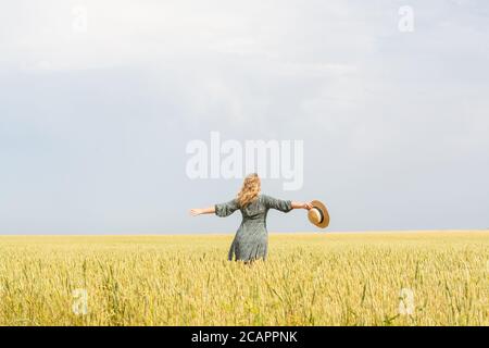 Femme en chapeau de paille marchant dans le champ de seigle sur jour d'été Banque D'Images