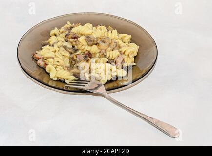 Assiette et fourchette transparentes avec pâtes spaghetti carbonara à la crème, champignons, bacon. Banque D'Images