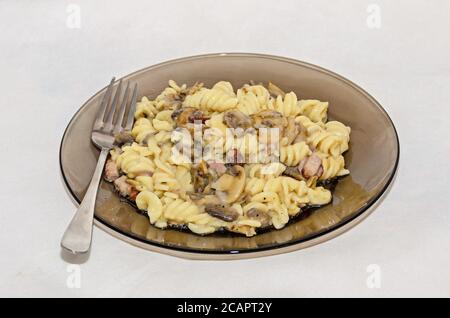 Assiette et fourchette transparentes avec pâtes spaghetti carbonara à la crème, champignons, bacon. Banque D'Images