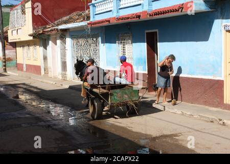 Deux hommes à cheval et à charrette, tandis qu'une femme balaie le trottoir, Trinidad, Cuba Banque D'Images