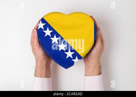 Drapeau de Bosnie-Herzégovine sur une boîte en forme de coeur dans les mains d'un homme. Arrière-plan blanc Banque D'Images