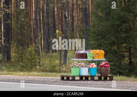 Récolte en vente (pomme de terre, champignons, pomme, baie différente) le long de la route, forêt de pins en arrière-plan. Commerce illégal sur les routes. Aliments biologiques Banque D'Images