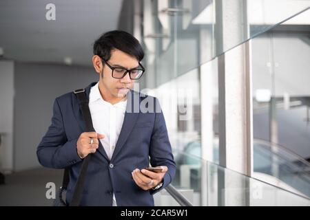 Les hommes d'affaires asiatiques utilisent des téléphones portables et vont en monter l'escalier roulant doit travailler le matin Banque D'Images