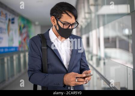 Les hommes d'affaires asiatiques portant un masque et utilisant leur téléphone et vont au travail le matin. Banque D'Images