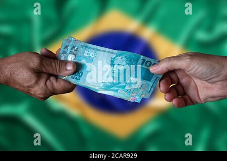 Billets d'argent brésiliens. Cent reais. Main de l'homme et main de la femme tenant une centaine de notes de reais avec drapeau brésilien flou de fond Banque D'Images