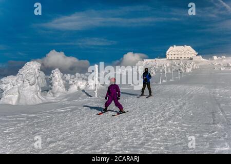 L'hiver, l'homme et l'enfant skent sous un vent fort près d'un refuge au sommet de Szrenica, dans le parc national de Karkonosze, à la frontière de la Pologne et de la République tchèque Banque D'Images