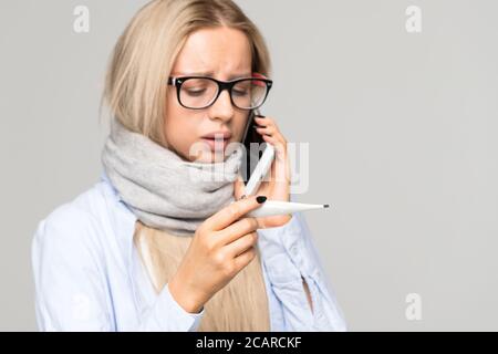 Une femme a attrapé le froid, regardant le thermomètre, vérifiant sa température corporelle, appelant le médecin par téléphone. Une femme contrariée se sent mal. Maladie, saison de la grippe Banque D'Images