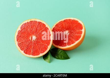 Deux moitiés de pamplemousse juteux mûr frais et deux feuilles sur fond vert menthe. Végétarien, régime alimentaire cru et alimentation saine. Antioxydant organique Banque D'Images