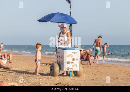 Punta Umbria, Huelva, Espagne - 7 août 2020 : une vendeuse de rue vend une glace à un enfant. Le vendeur porte un visage de protection ou médical Banque D'Images