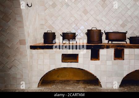 Ancienne cuisine carrelée de blanc propre avec poterie traditionnelle en cuivre et surface de cuisson en brique Banque D'Images