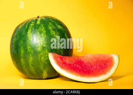 un melon d'eau entier et une tranche de pastèque sans graines sur fond jaune. thème d'été. fraîcheur. Délicieux melon d'eau mûr, juteux et rafraîchissant. Sucreries d'août. Banque D'Images