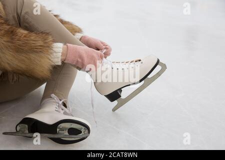 Gros plan de femme en fourrure et gants roses Patins blancs sur la patinoire en hiver. Femme nouant des patins. Week-ends activités à l'extérieur dans froid nous Banque D'Images