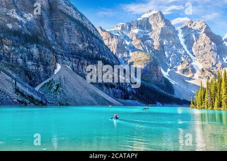 Des visiteurs non identifiables font du canoë sur leurs bateaux sur le lac Moraine de couleur turquoise dans les Rocheuses canadiennes du parc national Banff, près du lac Louise. Le va Banque D'Images