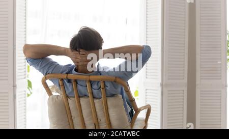 Vue arrière calme rêveur jeune homme se reposant sur une chaise confortable Banque D'Images