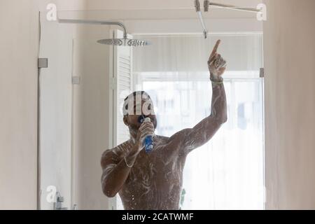 Homme afro-américain positif s'amusant dans la salle de bains, chantant Banque D'Images